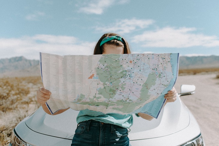 Woman standing in front of her car looking at a road map