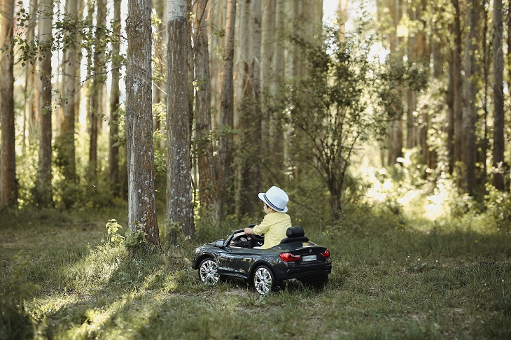 Child sitting in a toy car and driving through the forest
